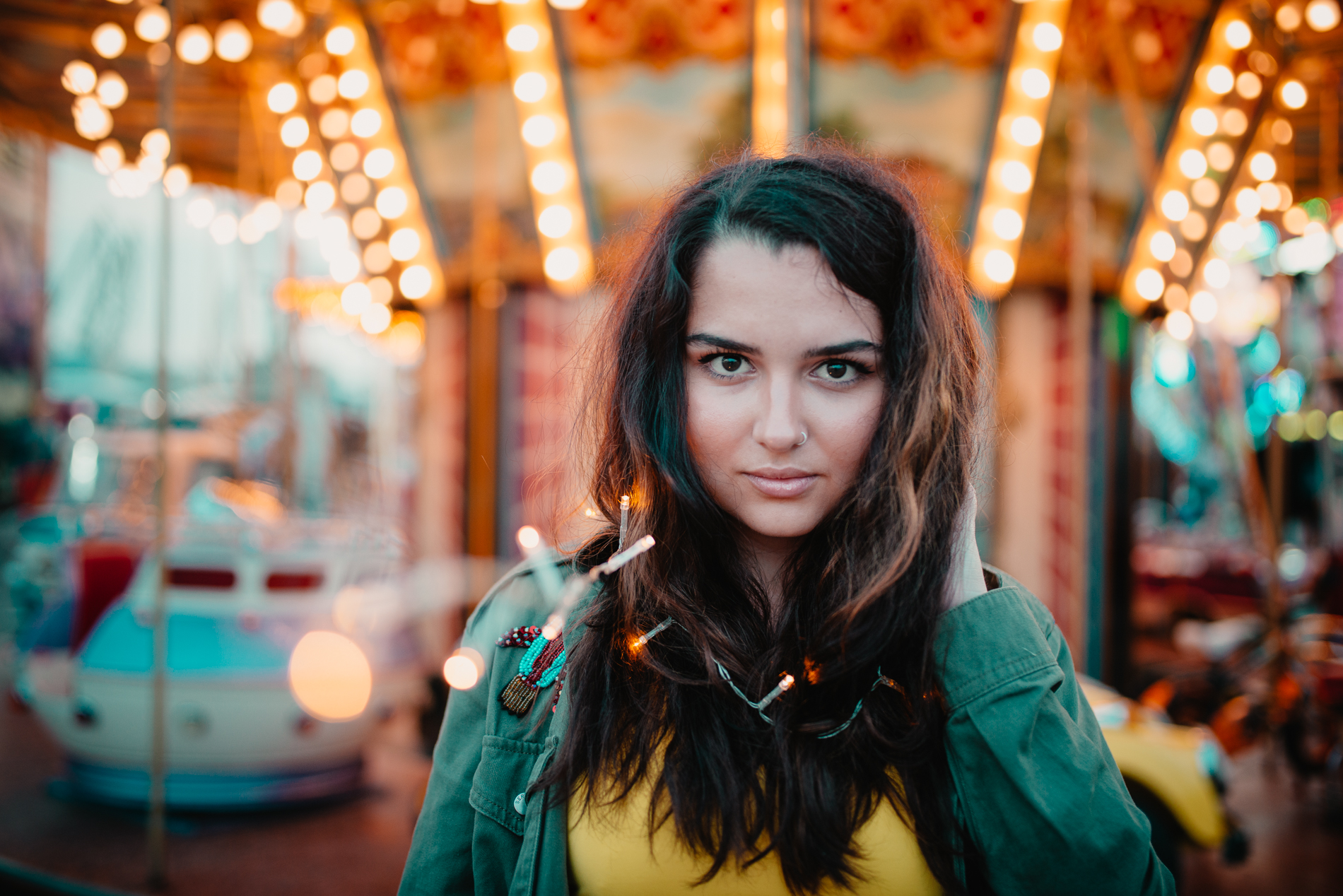 girl portrait in a fair next to a carrousel with bokeh lights